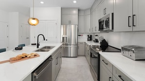 Une cuisine moderne dotée d’appareils électroménagers en acier inoxydable, d’un plan de travail blanc et d’un luminaire suspendu.