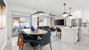 A modern kitchen with white cabinets, a large island, and a dining area with a round table and chairs. - Rory’s Residence | Instaworthy home near parks w social media BR, pool, luxe BRs (Orlando)