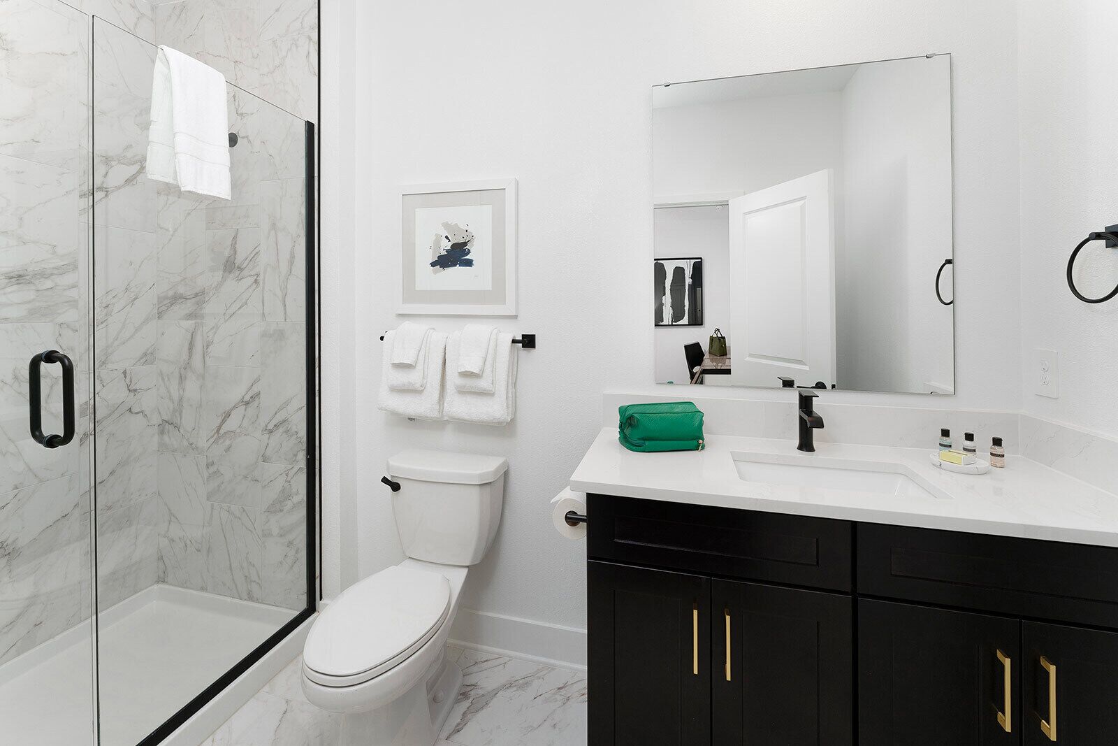 A modern bathroom with a glass shower enclosure, a toilet, a sink with a mirror, and black cabinets.
