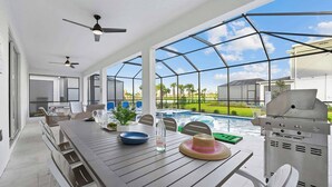 Un espace repas extérieur moderne avec vue sur la piscine, un barbecue et des ventilateurs de plafond.