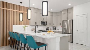 Une cuisine moderne dotée d’un îlot central, de tabourets de bar, d’appareils électroménagers en acier inoxydable et de luminaires suspendus.