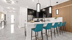 Une cuisine moderne avec un îlot central blanc, des meubles de rangement noirs et des tabourets de bar de couleur turquoise.