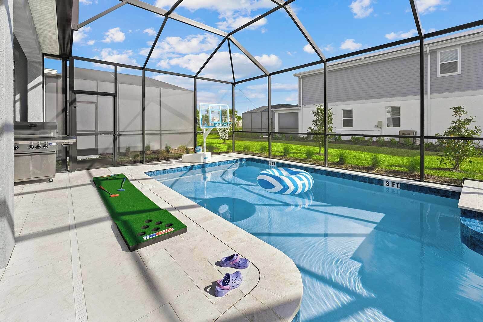 Uma área de piscina com mesa de pebolim verde, boia inflável azul e branca e mesa de bilhar.