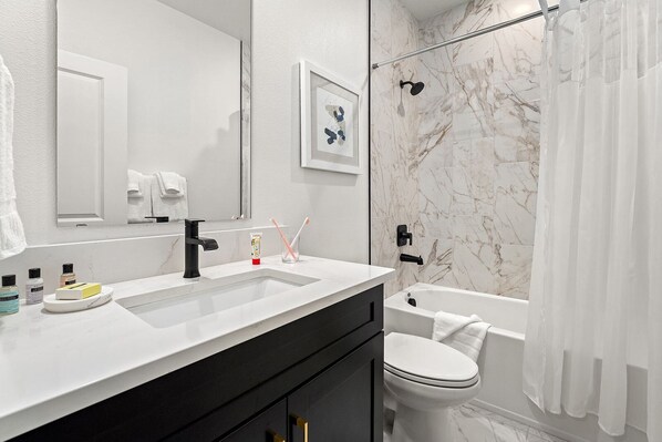 A modern bathroom with a white marble shower, a black sink, and a white toilet.