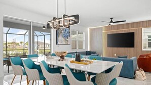 A modern dining area with a white table, teal chairs, and a decorative bowl centerpiece. - Majestic Marvel | Showstopping estate on I-Drive w/ 2 theme RMs, theater, arcade (Orlando)