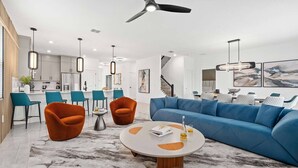 A modern living room with a blue sofa, orange armchairs, and a marble coffee table. - Majestic Marvel | Showstopping estate on I-Drive w/ 2 theme RMs, theater, arcade (Orlando)