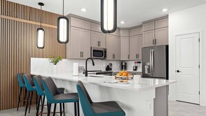 A modern kitchen with a central island, bar stools, stainless steel appliances, and pendant lighting. - Majestic Marvel | Showstopping estate on I-Drive w/ 2 theme RMs, theater, arcade (Orlando)