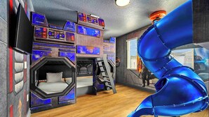 Una habitación con una cama litera, un tobogán en espiral y una pared con varios monitores.