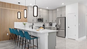 Una cocina moderna con una isla central, taburetes de bar, electrodomésticos de acero inoxidable y una pared decorativa de madera.