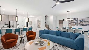 Una sala moderna con un sofá azul, sillones naranjas y una mesa de centro redonda.