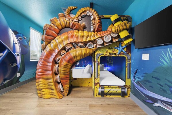 A room with a large octopus play structure, a small bed, and a wall mural of a sea scene.