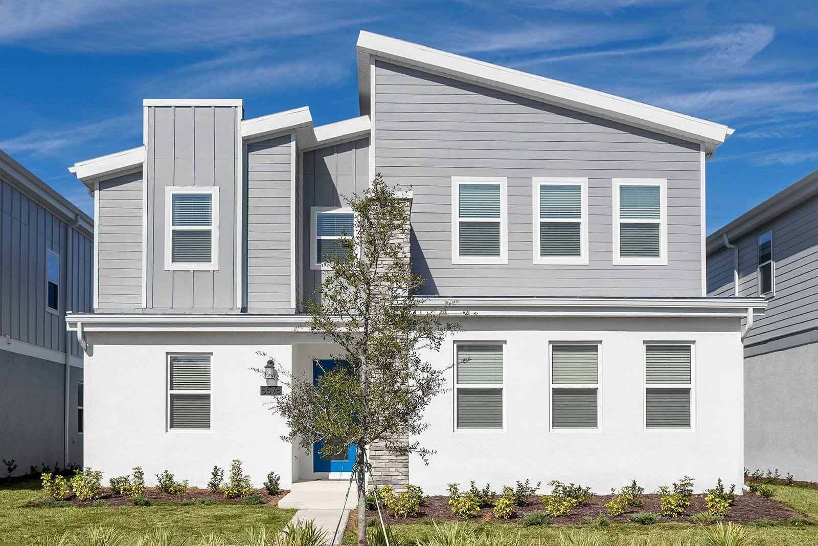 A modern two-story residential building with a blue door, white siding, and multiple windows with shutters.