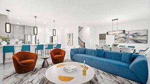 Een moderne woonkamer met een blauwe bank, twee oranje fauteuils en een ronde salontafel.