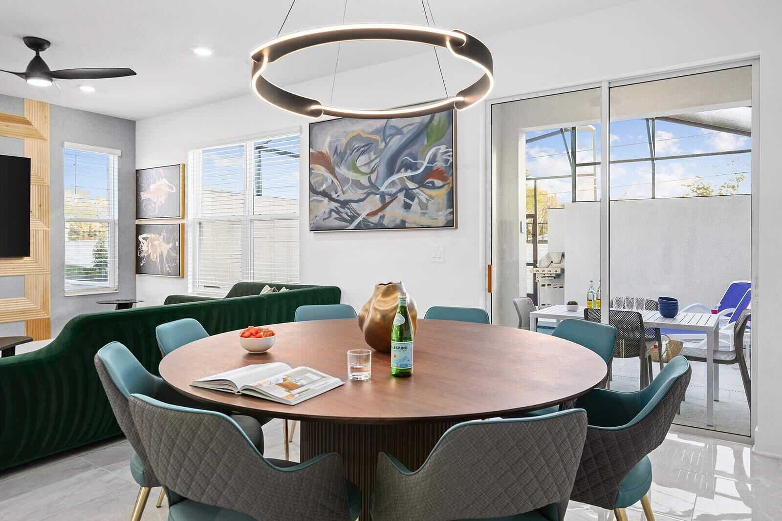 A modern dining area with a round table, green upholstered sofas, and a large abstract painting on the wall.