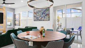A modern dining area with a round table, green upholstered sofas, and a large abstract painting on the wall.