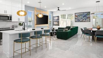 A modern kitchen with a central island, bar stools, a green sofa, and a dining area with chairs and a table.