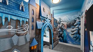 Een kamer met een muurschildering in kasteelthema, een groot raam en een stenen muur.