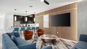 Een moderne woonkamer met een bank, twee fauteuils, een salontafel en een aan de muur bevestigde televisie.