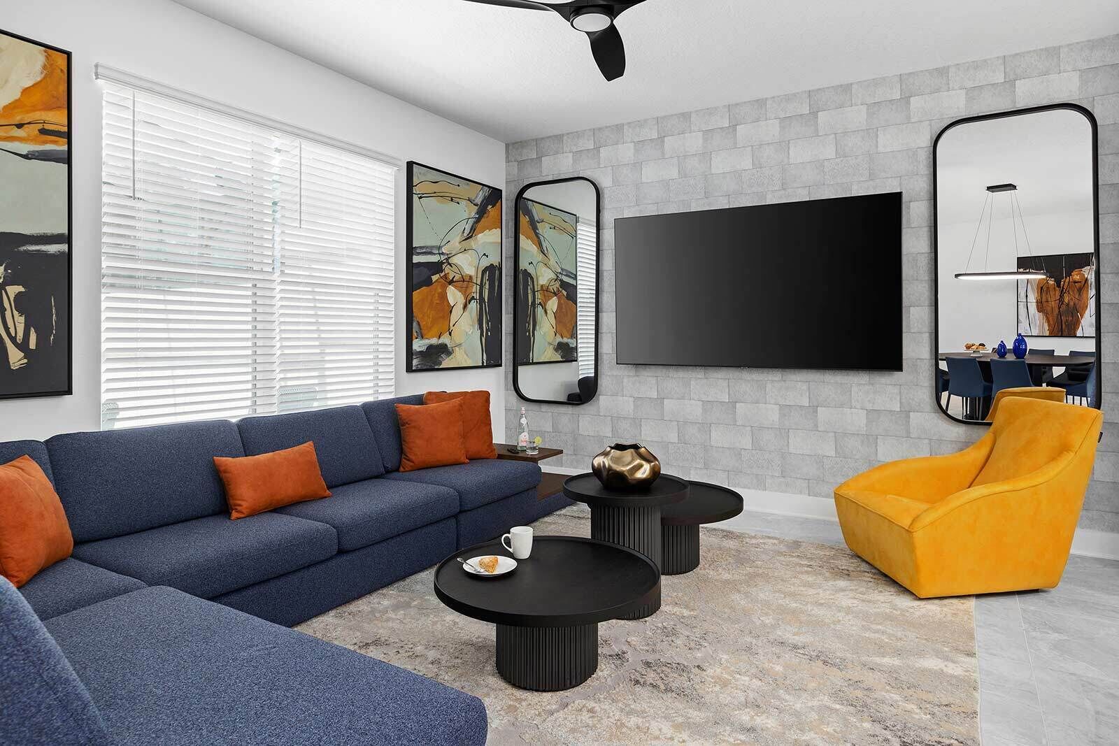 Una sala de estar moderna con un sofá azul, dos mesas de centro negras, un sillón amarillo y obras de arte en las paredes.