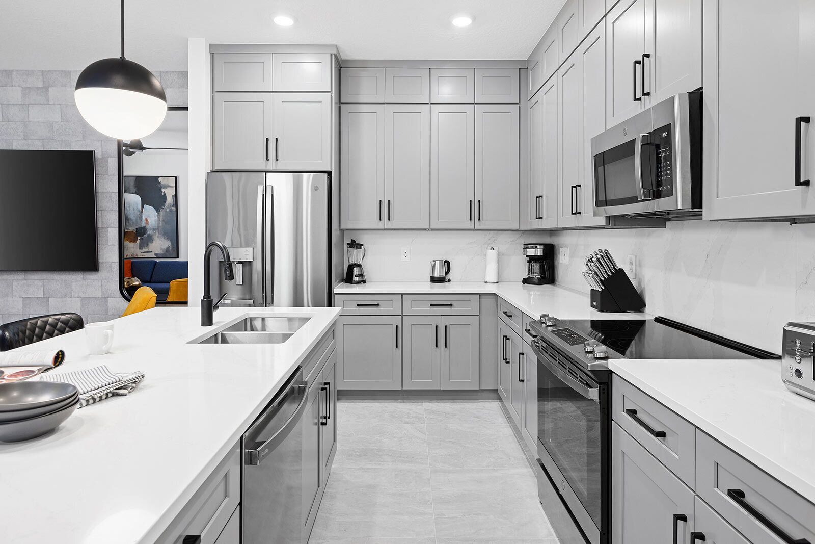 A modern kitchen with stainless steel appliances, grey cabinetry, and a large island with a sink.