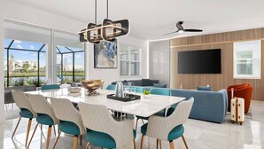 A modern living room with a dining area, large windows, and a flat-screen TV. - Wondrous Wonderland | A dream escape on I-Drive - theme RMs, PVT pool, theater (Orlando)