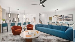 A modern living room with a blue sofa, orange chairs, a round coffee table, and a kitchen in the background. - Wondrous Wonderland | A dream escape on I-Drive - theme RMs, PVT pool, theater (Orlando)