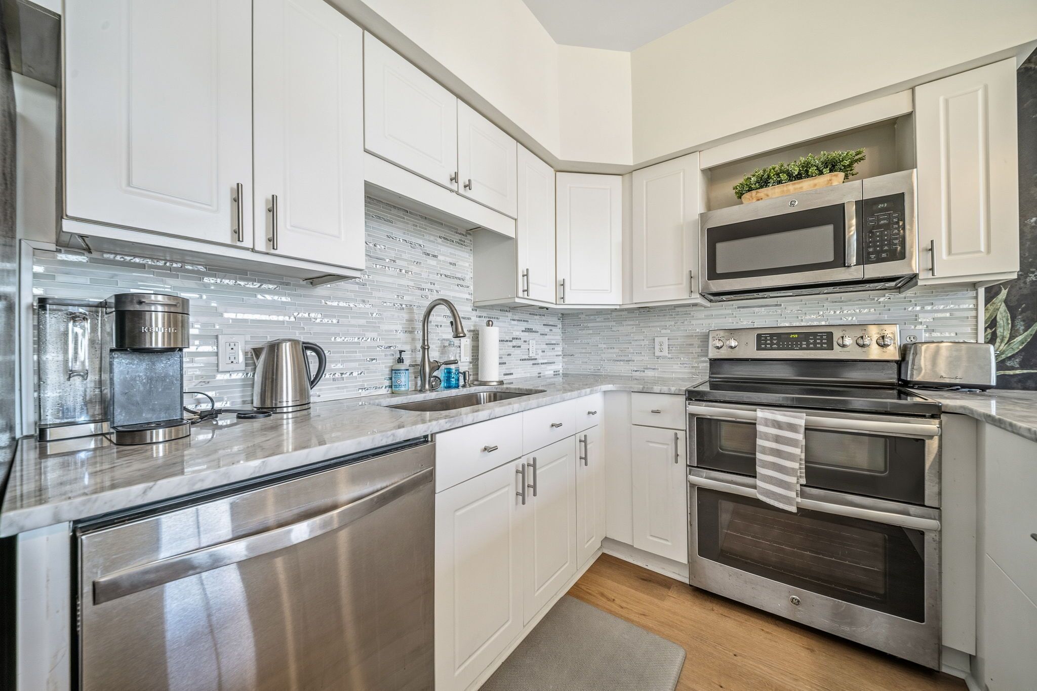 A modern kitchen with stainless steel appliances, white cabinetry, and a tiled backsplash.
