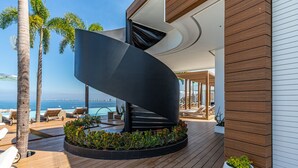 A modern outdoor area with a curved black structure, wooden deck, lounge chairs, and a view of the sea. - Largest Rooftop Pool in Latin America! (Puerto Vallarta)