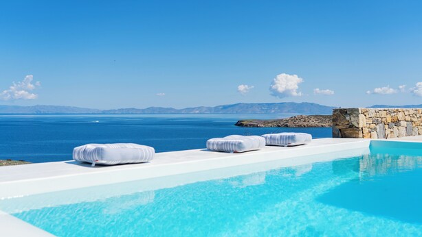 An infinity pool with white loungers and a stone wall, overlooking a clear blue sea and distant mountains. - Villa Cycladic View Syros  (Azolimnos Syros)