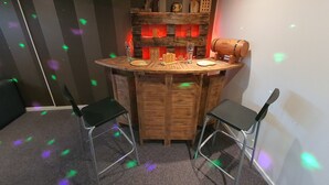 Eine gemütliche Bar mit einer Holztheke, zwei Metallstühlen und einer Flaschen- und Gläserauslage.