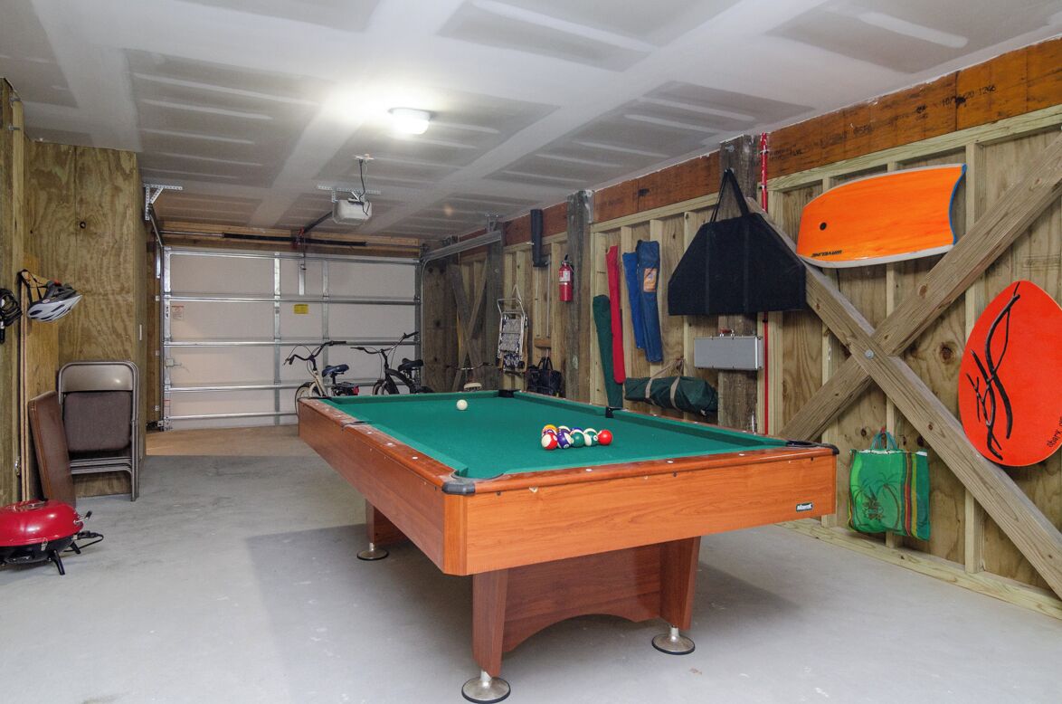 A pool table in a room with a wooden wall and a garage door in the background.