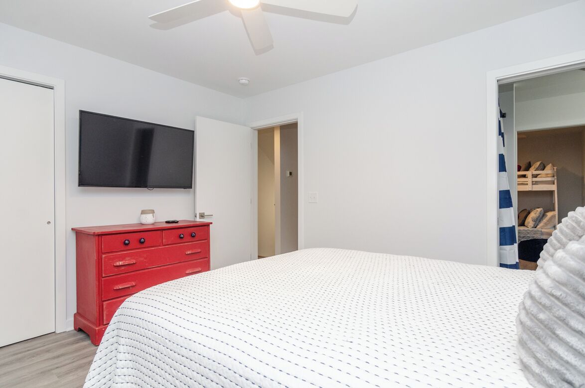Een slaapkamer met een bed, een rode ladekast, een televisie en een kast met een gestreept gordijn.