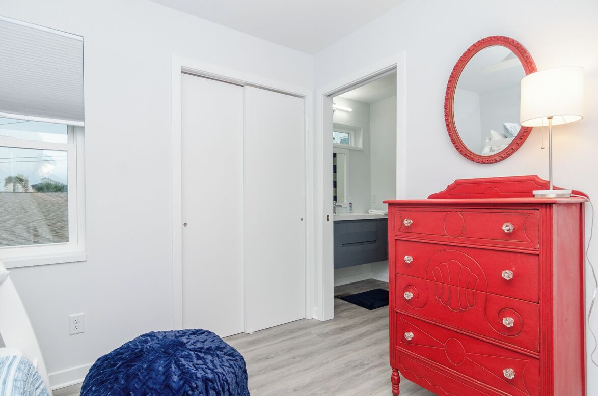 A room with a red dresser, a mirror, and a window.