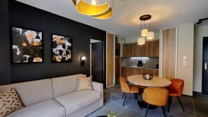 A modern living room with a sofa, a dining table with chairs, and a kitchen area with wooden cabinets. - Wifi, 100m from ski slopes, swimming pool, sauna, hammam, tv, ski locker, 37m², Auron (Auron)