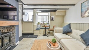Una sala de estar moderna con un sofá, una mesa de centro y una chimenea. Se ve un área de cocina con una mesa de comedor y sillas a través de una puerta abierta.