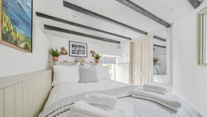 Un dormitorio con una cama grande, ropa de cama blanca, un espejo y vistas al exterior.