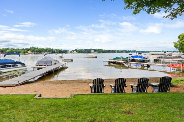 A lakeside dock with boats, a covered area, and a grassy area with chairs. - Lakefront Retreat on Powers Lake | Sandy Beach, Private Pier & Sunset Views (Genoa City)