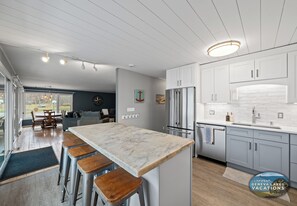 A modern kitchen with a marble countertop, stainless steel appliances, and wooden stools.