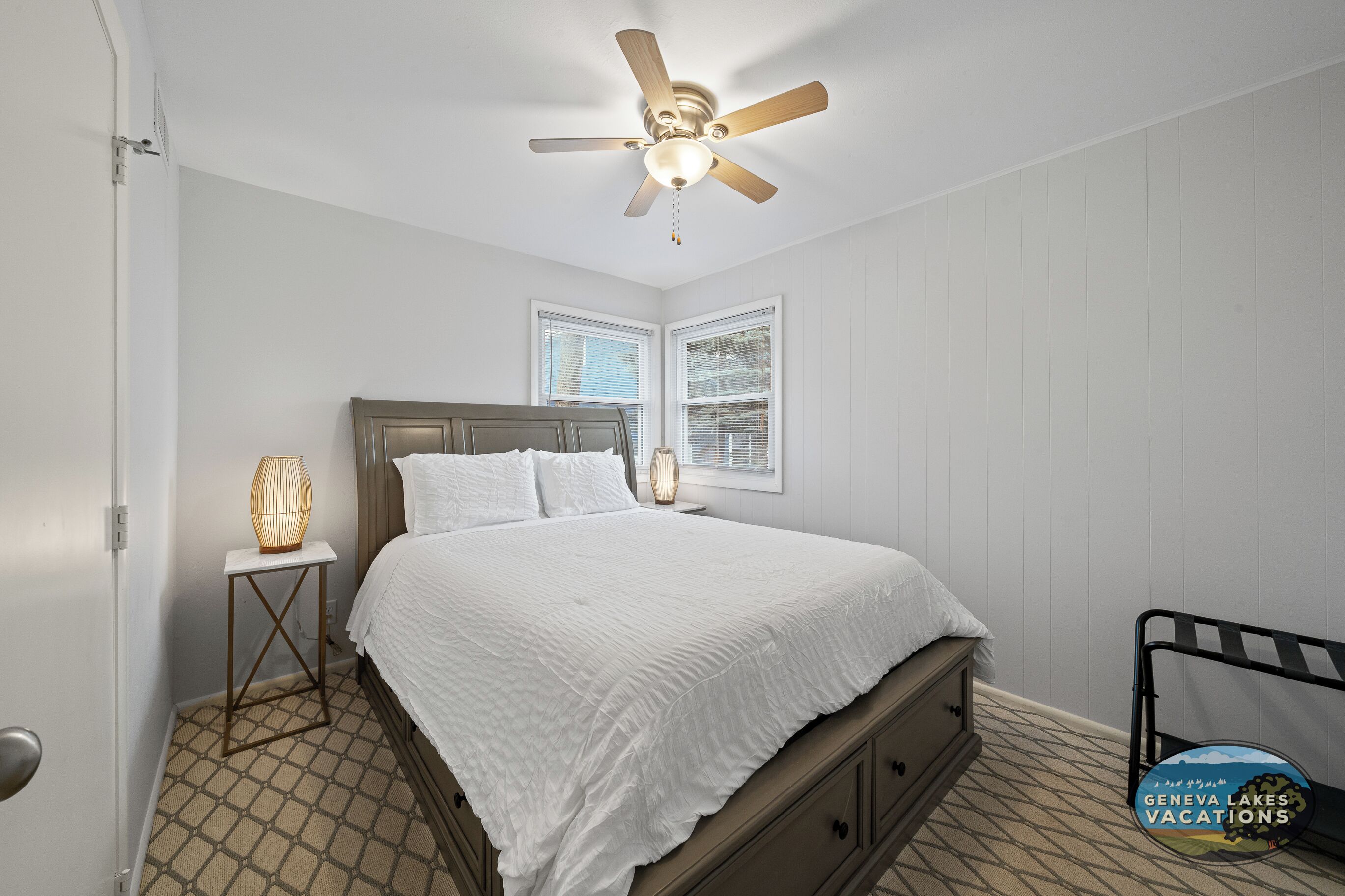 A bedroom with a bed, a nightstand, a ceiling fan, and a window.