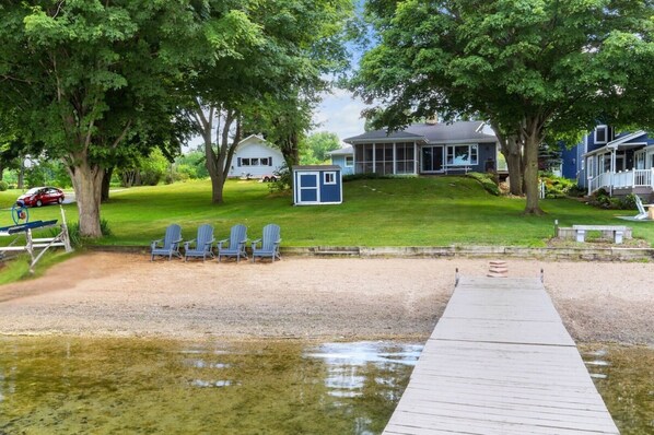 A lakeside property with a dock, a small shed, and a row of Adirondack chairs.