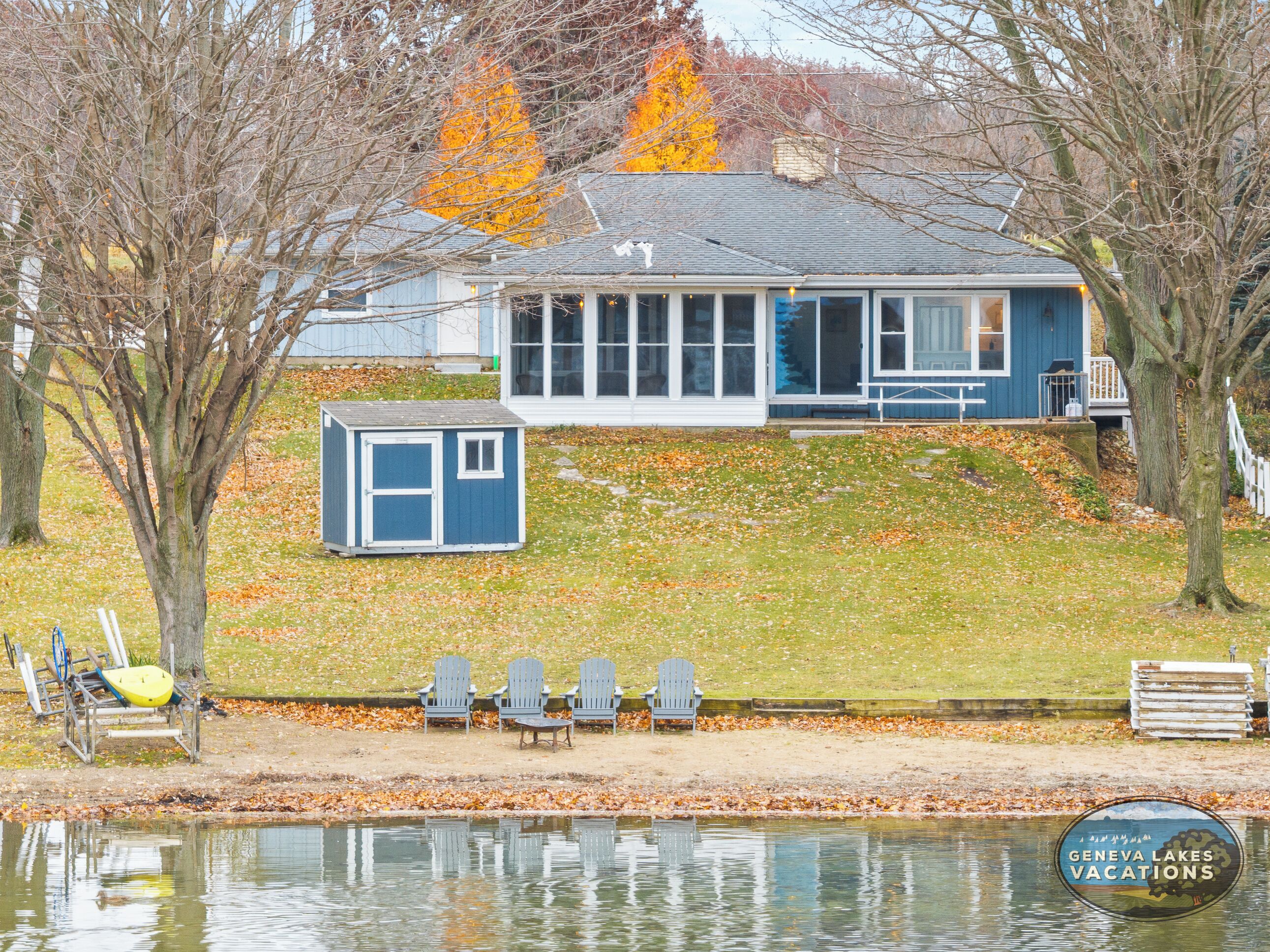 A lakeside cabin with a small dock and chairs by the water.