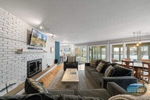A modern living room with a fireplace, a large TV, and a view of a lake.
