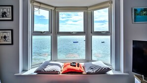 Un dormitorio con ventanal panorámico que da a una masa de agua, una cama con almohadas y un televisor sobre un mueble.