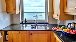 Una cocina con armarios de madera, encimera negra, un lavamanos y una ventana con vistas al agua.