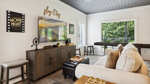 A modern living room with a herringbone-patterned cabinet, a large flat-screen TV, a sofa with cushions, a wooden coffee table, and a 'movie night' sign. - Sunset Chalet 2 Bedroom Cabin by RedAwning (Gatlinburg)