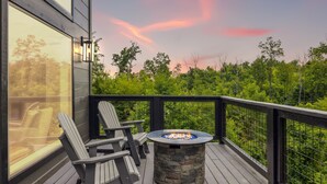 A deck with Adirondack chairs, a stone fire pit, and a view of a forest. - Sunset Chalet 2 Bedroom Cabin by RedAwning (Gatlinburg)