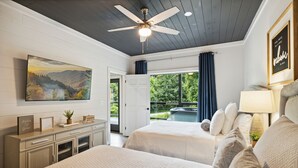 A bedroom with two beds, a ceiling fan, a painting, a desk with drawers, and a window with curtains. - Sunset Chalet 2 Bedroom Cabin by RedAwning (Gatlinburg)
