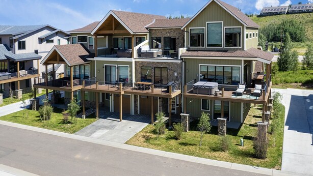 A modern multi-story residential building with a spacious deck area, large windows, and a hillside backdrop. - Hay Meadow Lodge 3 Bedroom Townhouse by RedAwning (Fraser)