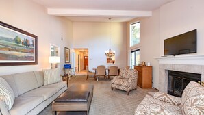 A living room with a sofa, ottoman, patterned armchair, and a fireplace.