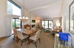 Amplia sala de estar con una gran mesa de comedor, asientos cómodos, chimenea y ventanas grandes que ofrecen vistas al exterior.